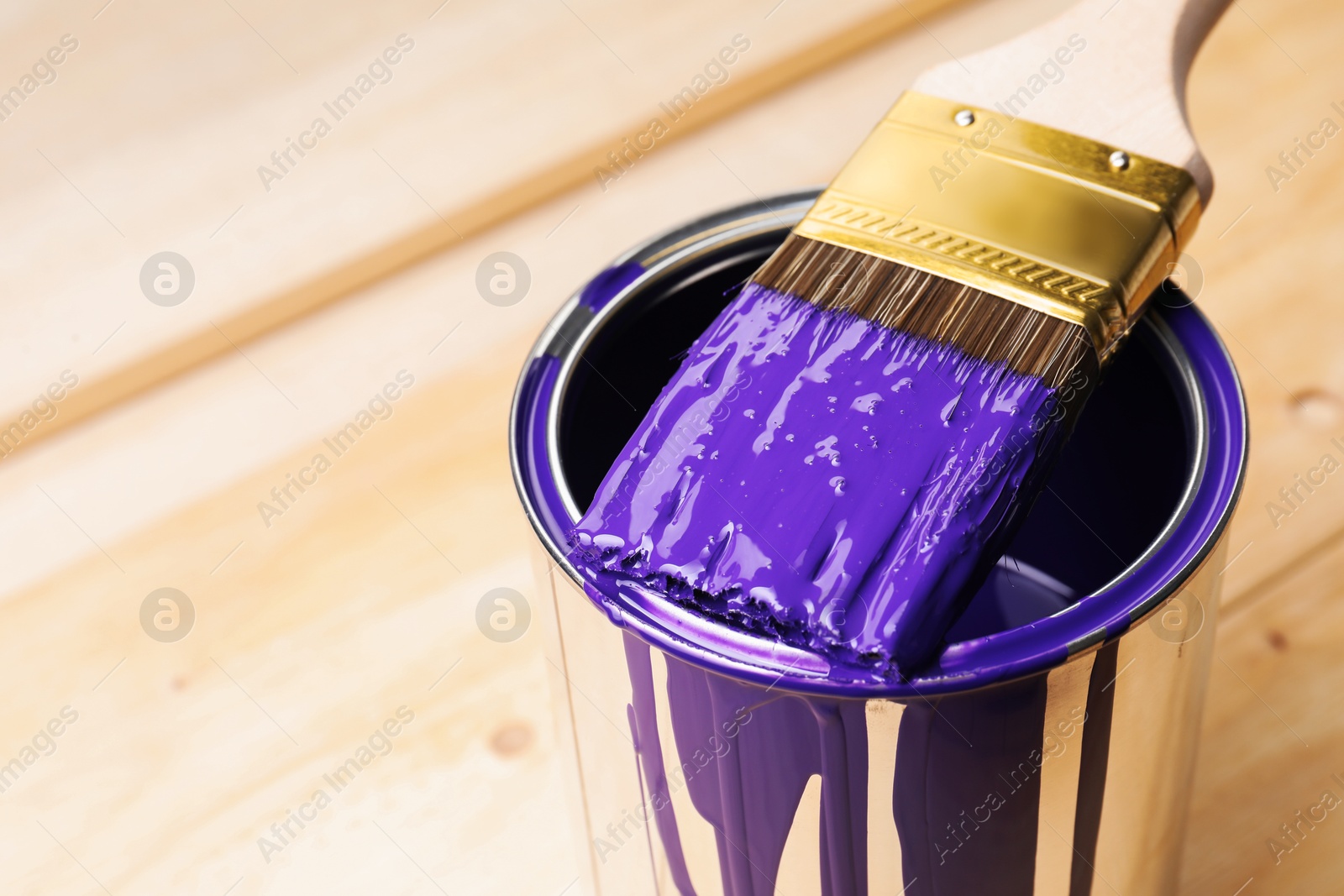 Photo of Can of purple paint and brush on wooden table, closeup. Space for text