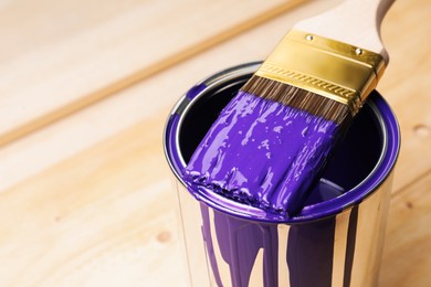 Photo of Can of purple paint and brush on wooden table, closeup. Space for text