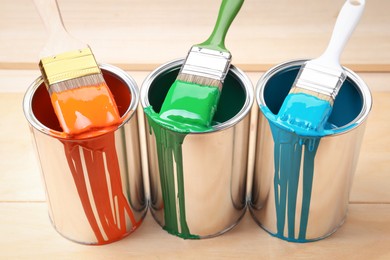 Photo of Cans of paint and brushes on wooden table, closeup