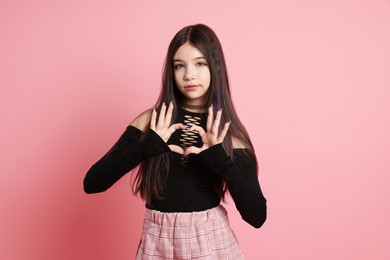 Photo of Teenage girl making heart gesture on pink background. Makeup and clothes in anime style