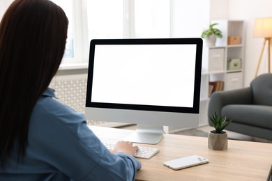 Photo of Woman looking at monitor with blank screen at wooden table indoors. Mockup for design