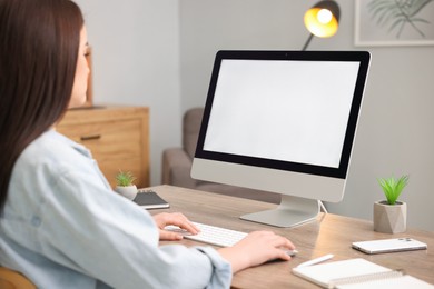 Photo of Woman looking at monitor with blank screen at wooden table indoors. Mockup for design