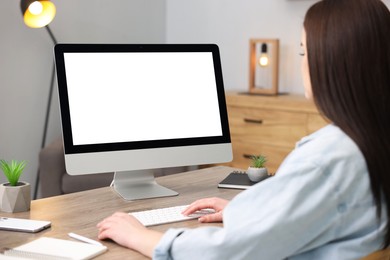 Photo of Woman looking at monitor with blank screen at wooden table indoors. Mockup for design