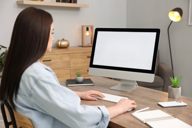 Photo of Woman looking at monitor with blank screen at wooden table indoors. Mockup for design