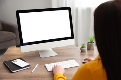 Photo of Woman looking at monitor with blank screen at wooden table indoors. Mockup for design