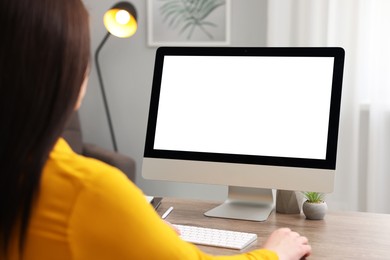 Photo of Woman looking at monitor with blank screen at wooden table indoors. Mockup for design