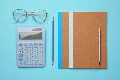 Photo of Copybooks, glasses and other different stationery on light blue background, flat lay