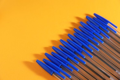 Photo of Many ballpoint pens with caps on orange background. Space for text