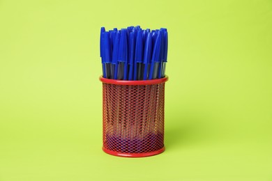 Photo of Many ballpoint pens in holder on green background