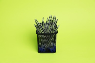 Photo of Many ballpoint pens in holder on green background