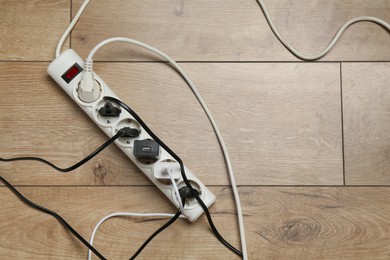 Photo of Extension power board overloaded with plugs on wooden floor, top view. Space for text