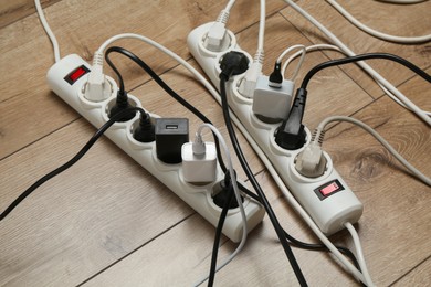 Photo of Extension power boards overloaded with plugs on wooden floor, closeup