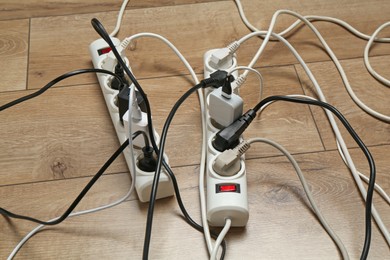 Photo of Extension power boards overloaded with plugs on wooden floor, closeup