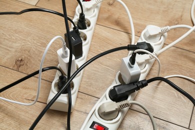 Photo of Extension power boards overloaded with plugs on wooden floor, closeup