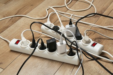 Photo of Extension power boards overloaded with plugs on wooden floor, closeup