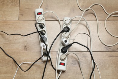 Photo of Extension power boards overloaded with plugs on wooden floor, top view