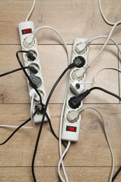 Photo of Extension power boards overloaded with plugs on wooden floor, top view