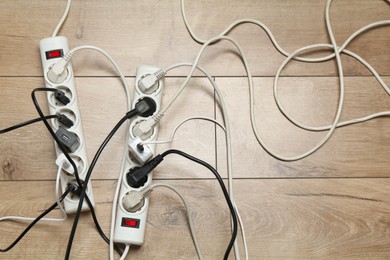 Photo of Extension power boards overloaded with plugs on wooden floor, top view