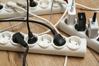 Photo of Extension power boards overloaded with plugs on wooden floor, closeup