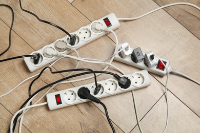 Photo of Extension power boards overloaded with plugs on wooden floor, top view