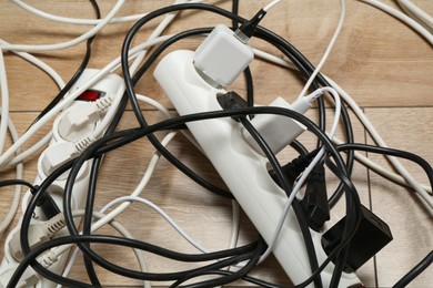 Photo of Extension power boards overloaded with plugs on wooden floor, closeup