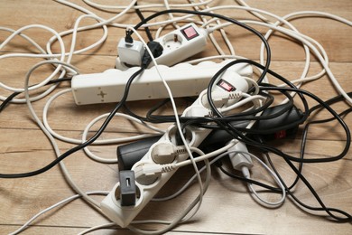 Photo of Extension power boards overloaded with plugs on wooden floor, closeup