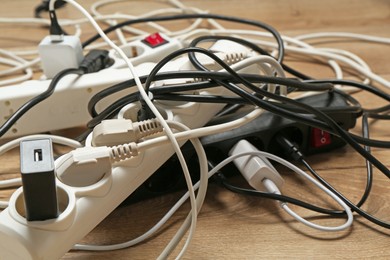 Photo of Extension power boards overloaded with plugs on wooden floor, closeup