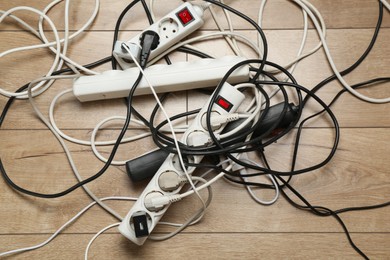 Photo of Extension power boards overloaded with plugs on wooden floor, top view