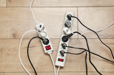 Photo of Extension power boards overloaded with plugs on wooden floor, top view