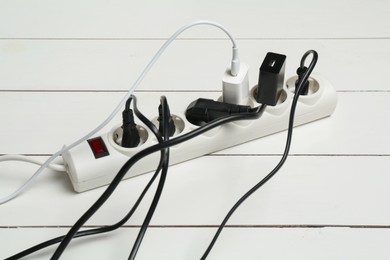 Photo of Extension power board overloaded with plugs on white wooden floor