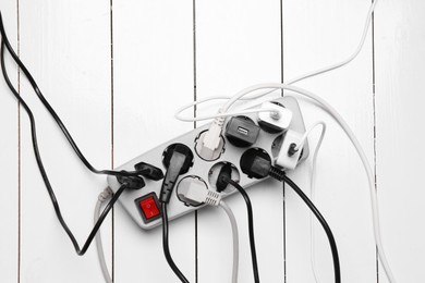 Photo of Extension power board overloaded with plugs on white wooden floor, top view