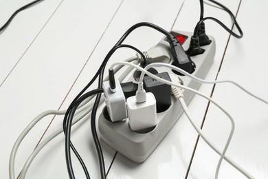 Photo of Extension power board overloaded with plugs on white wooden floor, closeup