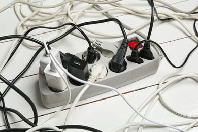 Photo of Extension power board overloaded with plugs on white wooden floor, closeup