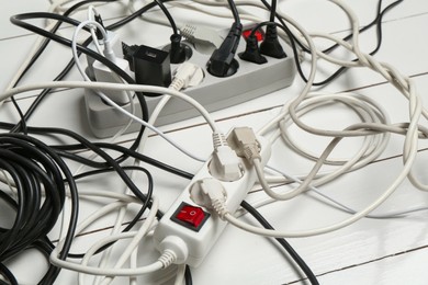 Photo of Extension power boards overloaded with plugs on wooden floor, closeup