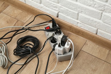 Photo of Extension power board overloaded with plugs on wooden floor, closeup