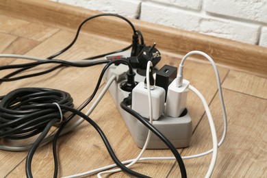 Photo of Extension power board overloaded with plugs on wooden floor, closeup