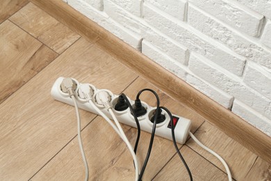 Photo of Extension power board overloaded with plugs on wooden floor, above view