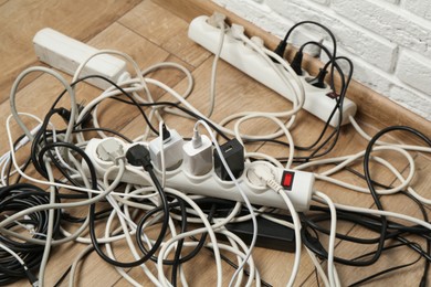 Photo of Extension power boards overloaded with plugs on wooden floor, closeup