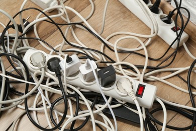 Photo of Extension power boards overloaded with plugs on wooden floor, closeup