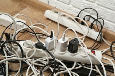 Photo of Extension power boards overloaded with plugs on wooden floor, closeup