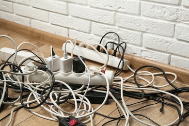 Photo of Extension power boards overloaded with plugs on wooden floor, closeup