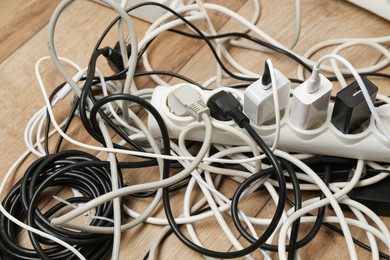 Photo of Extension power boards overloaded with plugs on wooden floor, closeup