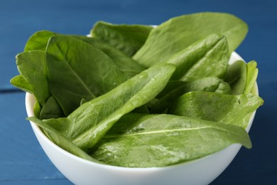 Photo of Fresh green sorrel leaves in bowl on blue table, closeup