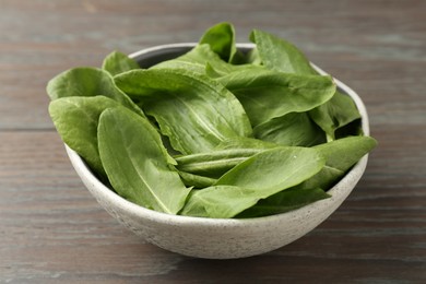 Photo of Fresh green sorrel leaves in bowl on wooden table, closeup