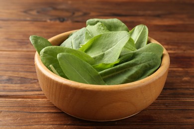 Photo of Fresh green sorrel leaves in bowl on wooden table, closeup