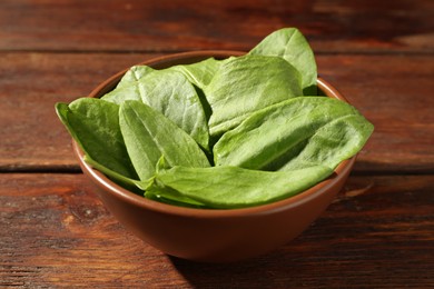 Photo of Fresh green sorrel leaves in bowl on wooden table, closeup