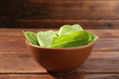 Photo of Fresh green sorrel leaves in bowl on wooden table, closeup