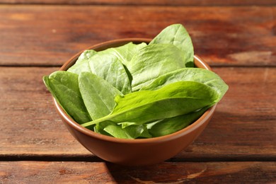 Photo of Fresh green sorrel leaves in bowl on wooden table, closeup