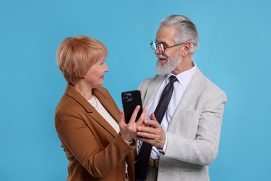 Photo of Lovely senior couple with smartphone on light blue background