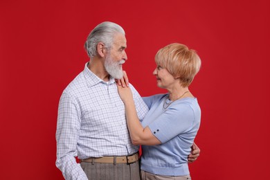 Photo of Lovely senior couple looking at each other on red background